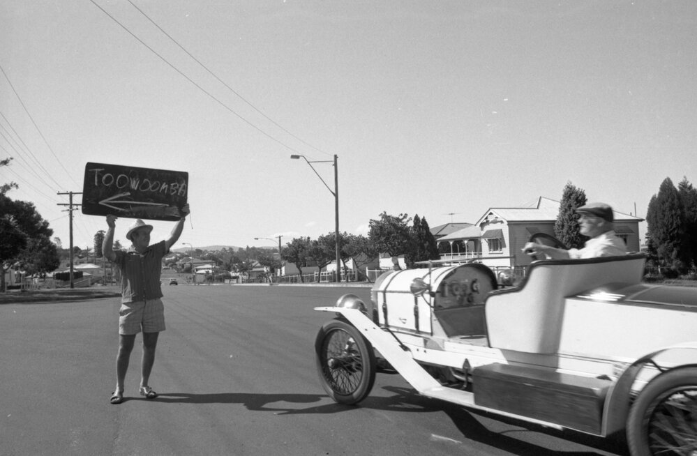 Man holding directional sign to Toowoomba at driver of vintage car, Ipswich, April 1978