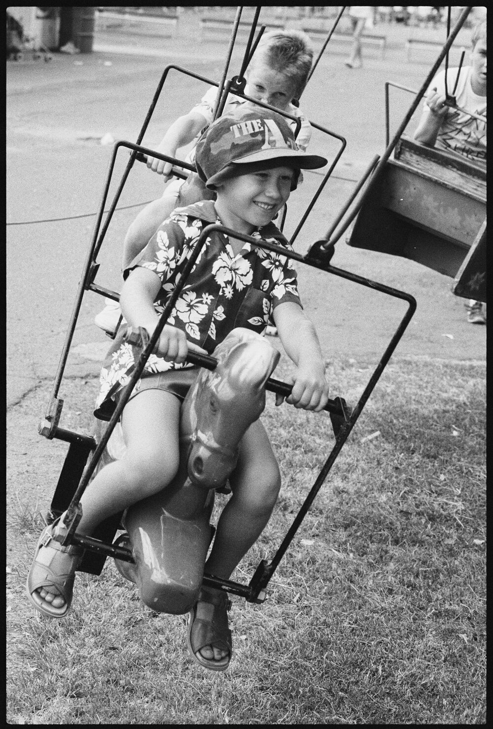 Boy in A-Team hat with other children on a swinging carnival ride at Ipswich Turf Club, Bundamba, January 1986