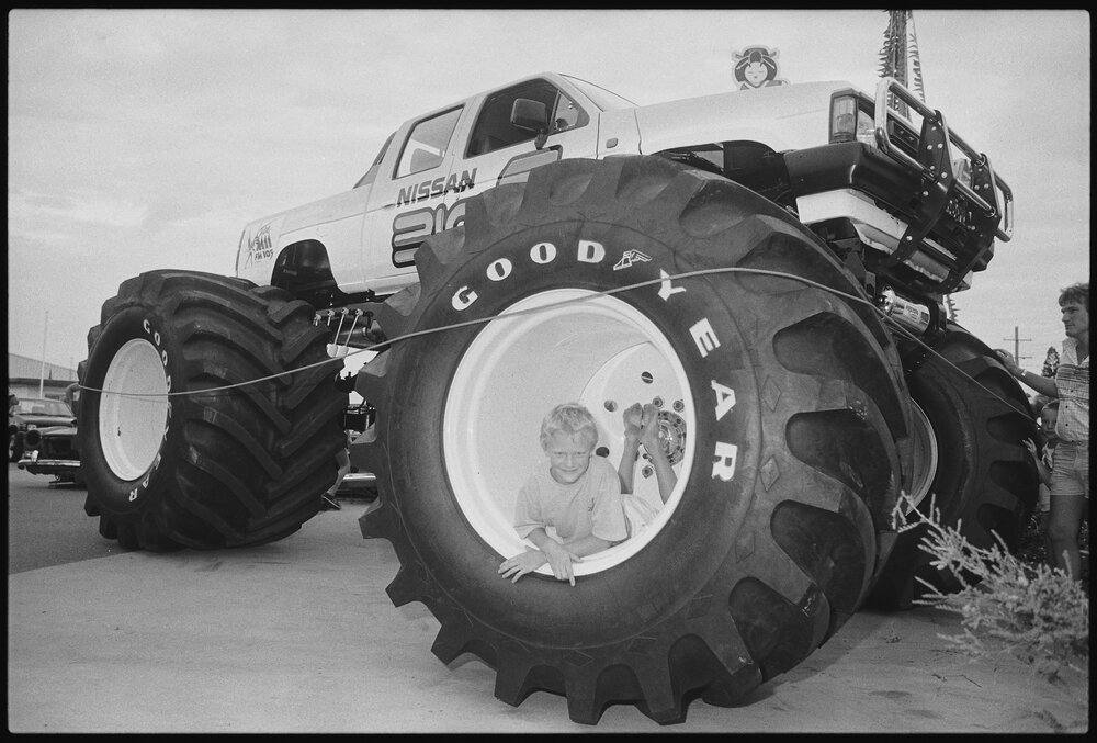 Unidentified boy in wheel of Nissan BIG-1 Monster Truck for exhibition at Ipswich Nissan car dealership, Booval, Ipswich, January 1986