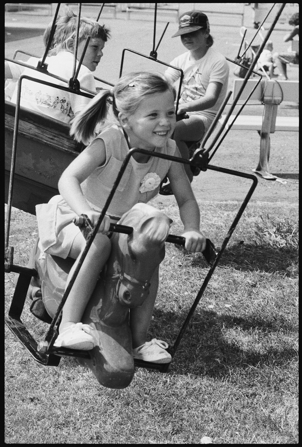 Little girl with pigtails and other children on a swinging carnival ride at Ipswich Turf Club, Bundamba, January 1986