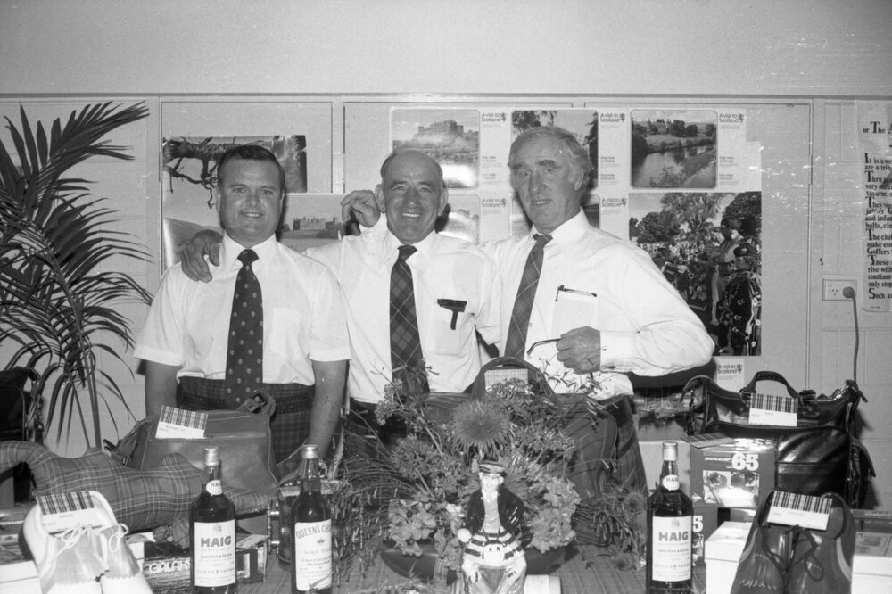 Three unidentified kilted men and one woman with a display about Scottish culture, Ipswich, September 1980