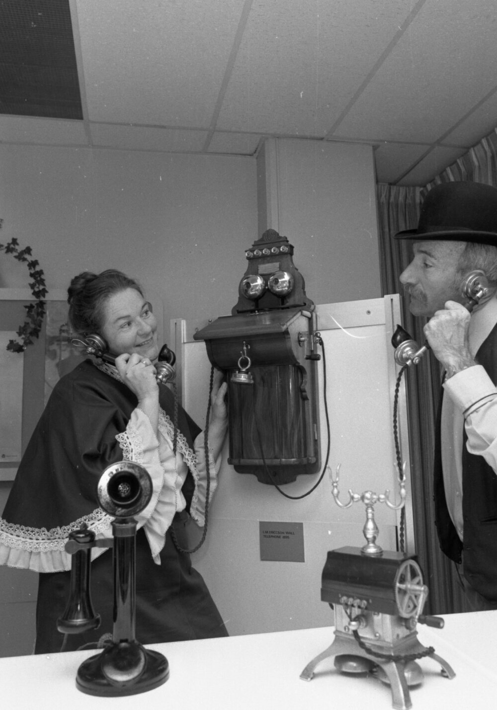 Unidentified man and woman in historical costume demonstrating an antique telephone at a Telecom Display, Ipswich, September 1980