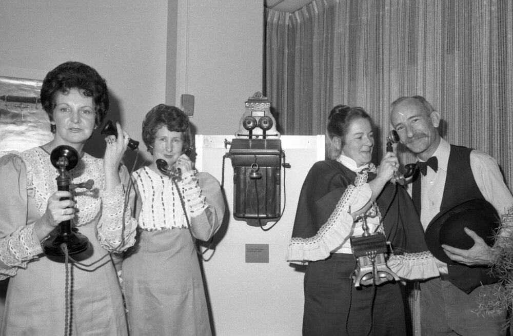 Three unidentified women and a man in historical costume demonstrating an antique telephone at a Telecom Display, Ipswich, September 1980