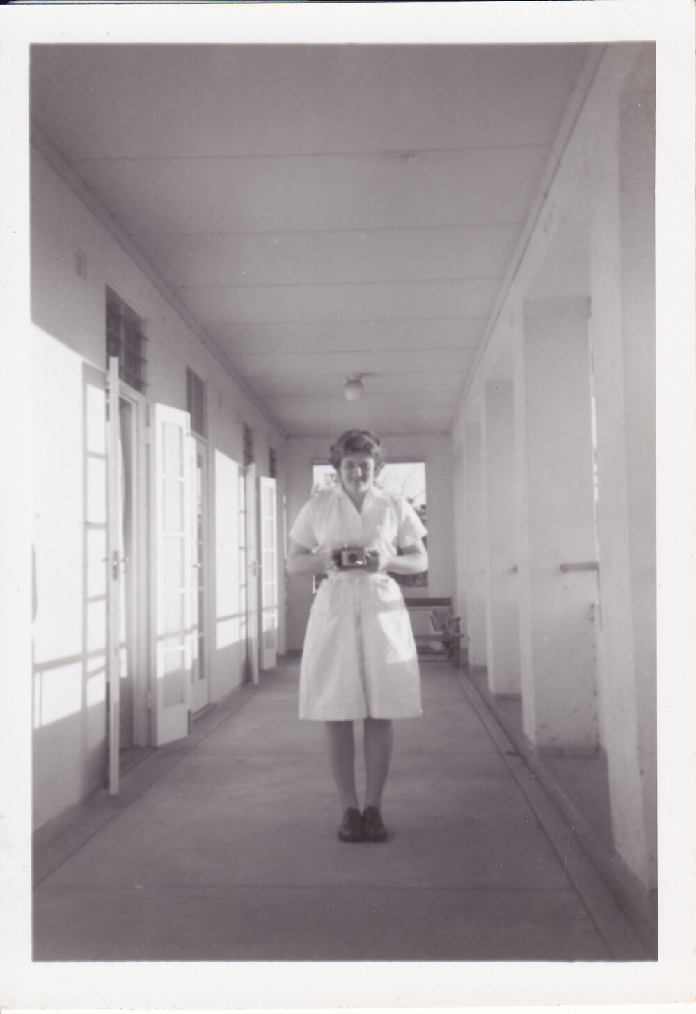 Nurse Monica Shine with camera on the verandah outside Trumpy House, 1950s