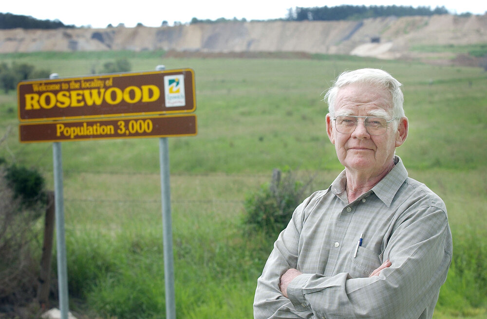 Arnold Rieck, standing beside the "Welcome to Rosewood" sign, Rosewood, Ipswich, March 2003
