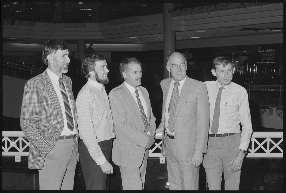 Unidentified group of men in business attire standing in front of the north escalator of Redbank Plaza Shopping Centre, Redbank, September 1985