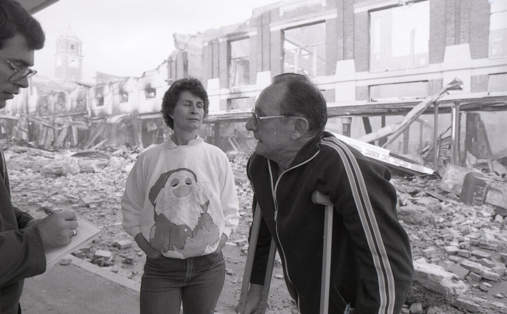 Man and woman being interviewed viewing the aftermath of the Reid's (Cribb &amp; Foote) fire, Bell Street, Ipswich, August 1985
