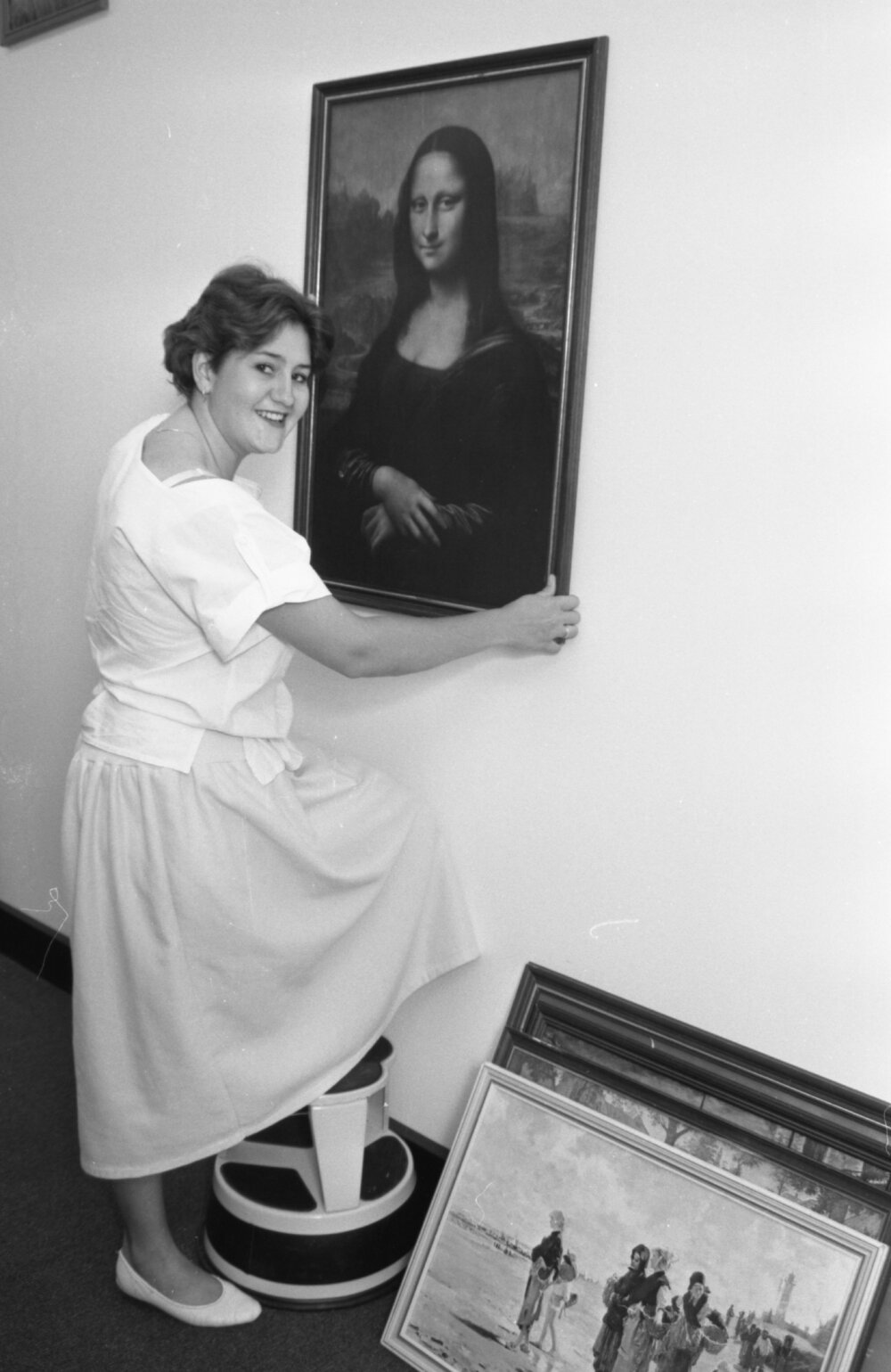 Unidentified library staff member hanging a poster of Leonardo da Vinci's 'Mona Lisa' in the Redbank Plaza Library, Redbank, September 1985