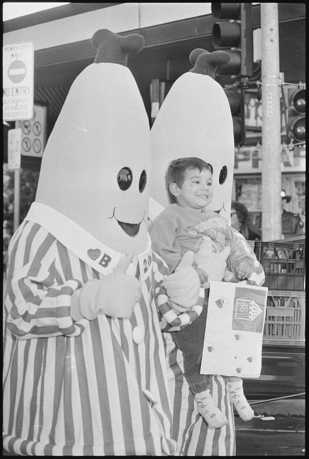 Bananas in Pyjamas are walking down Brisbane Street, Bananas in Pyjamas are carrying a small child, because in August 1994 the Variety Bash came to Ipswich