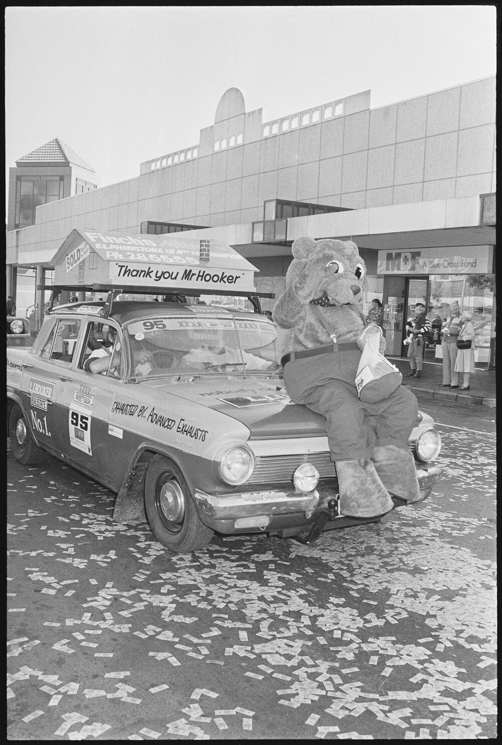 L.J. Hooker real estate bear mascot riding on the bonnet of the company's sponsored vehicle as part of the Variety Bash parade, Brisbane Street, Ipswich, 5th August 1994 