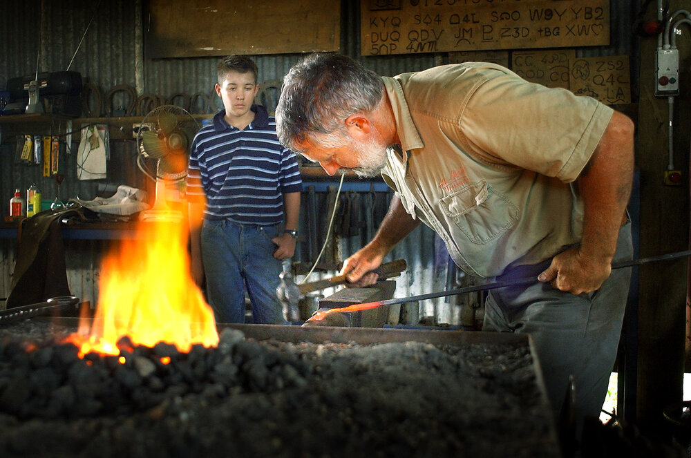 Blacksmith Alan Morris works on a piece of hot steel as his son Jeffery looks on, Ipswich, 18th January 2005 