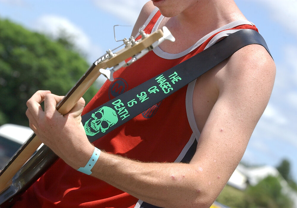 Not so subtle message on the guitar strap of the bass player from Christian rock band Soljah at Sonfest, Ipswich, 20th January 2005