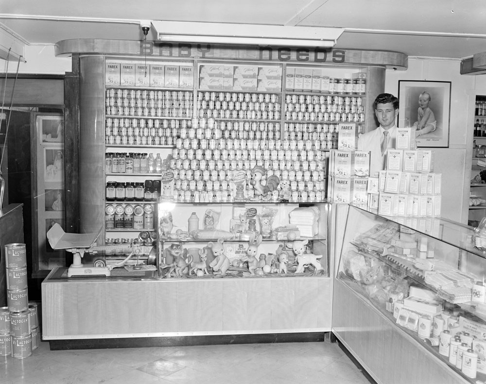 Staff member with Nolan's Pharmacy Baby Products display, corner of Brisbane and Nicholas Streets, Ipswich, 1955