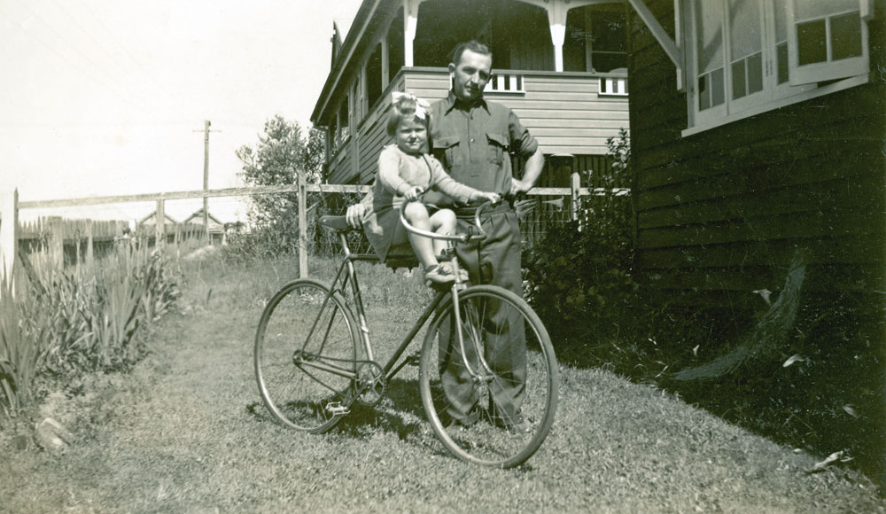 Young child on bicycle with her father at their home in Delacey Street, North Ipswich, 1949