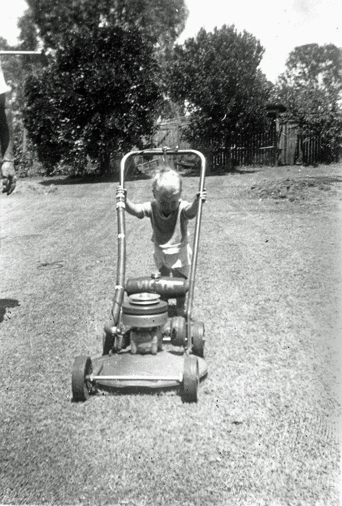 Young child pushing a Victa Motor Mower, 13 Hunter Street, Brassall, Ipswich, c.1950