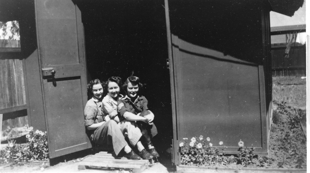 Three servicewomen posing in front of a small fibro shed at the Amberley Airbase, 1943