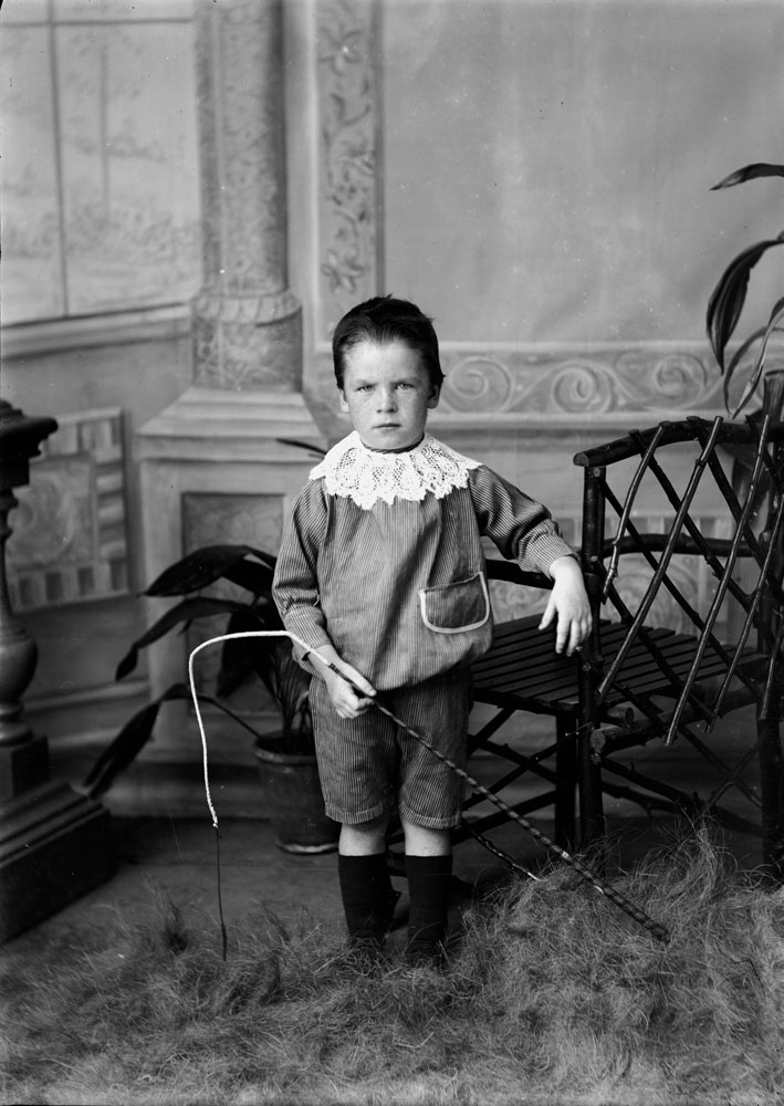 Studio portrait of unidentified young boy, wearing a striped suit with Young lace collar and holding a horse whip, I.X.L. Studios, Ipswich, 1900s.