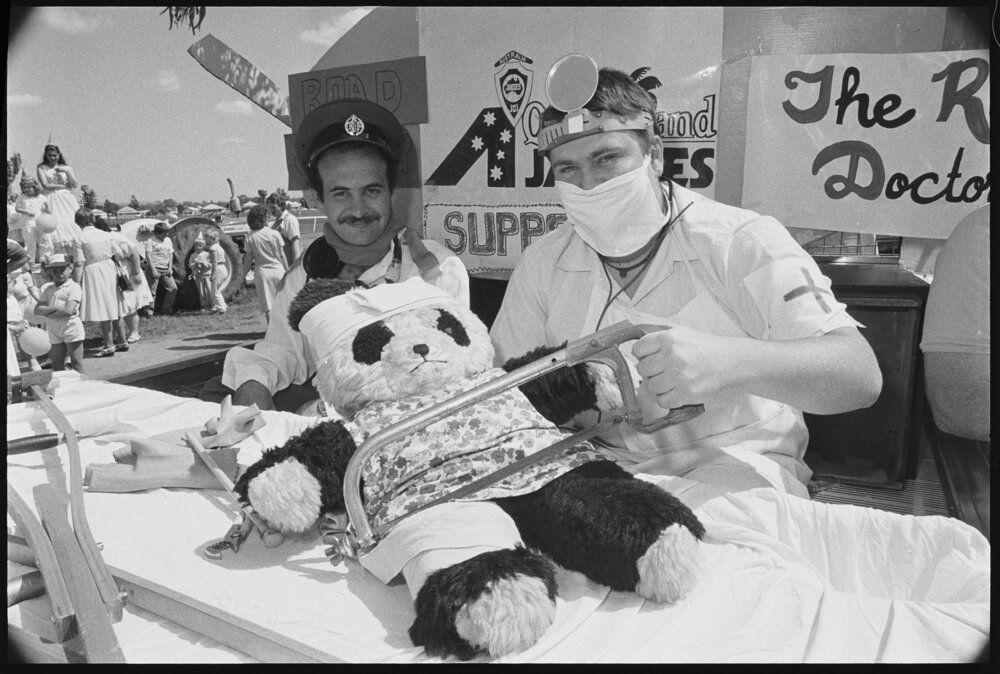 Two men in costume perform surgery on panda plush toy on a parade float at the Laidley Spring Festival, Laidley, Lockyer Valley, September 1987