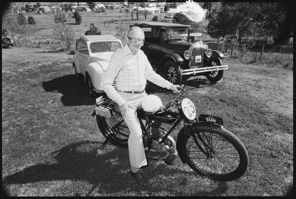 Unidentified man riding 1916 Sun motorcycle with 1926 Willys-Overland Whippet 2 Door Sedan car and 1951 Hartnett Pacific car, Ipswich, September 1987
