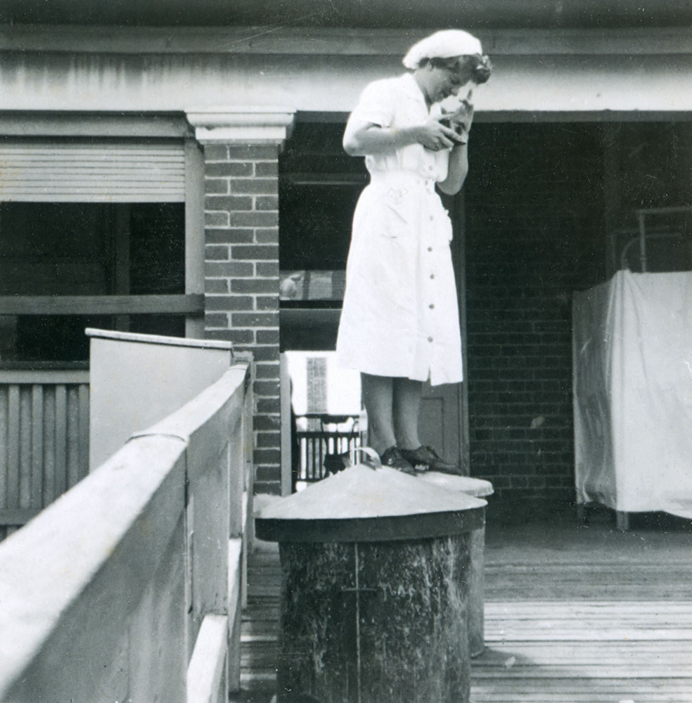 Nurse standing on garbage bin to take a photograph at Ipswich General Hospital, Ipswich, 1950s