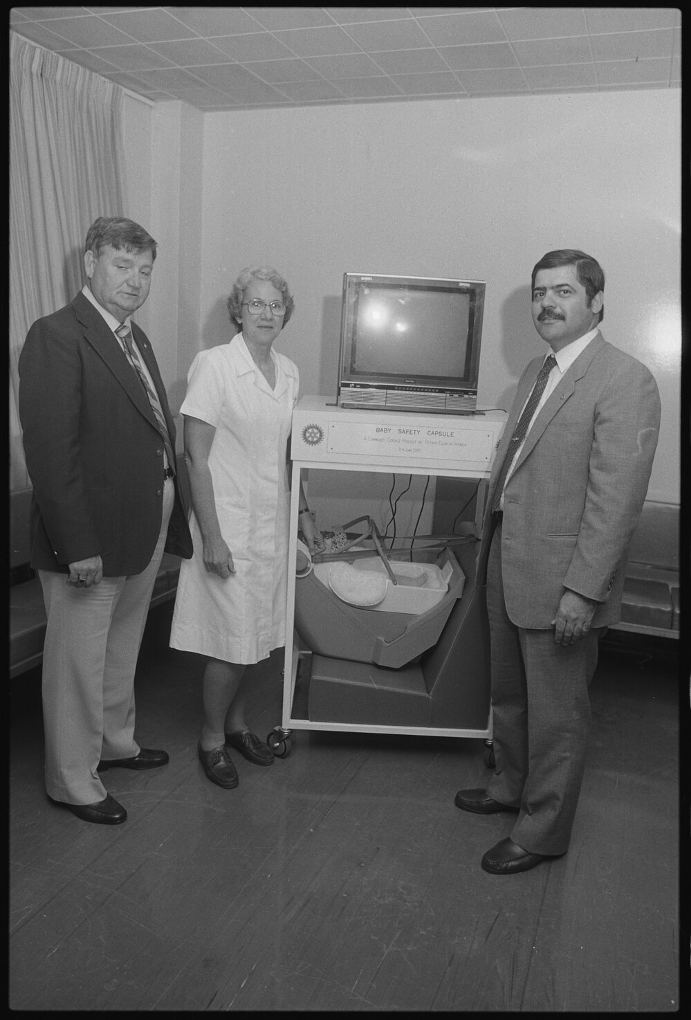 Dr Vlas Efstathis, a Nursing Sister and an unidentified man presenting a Ipswich Rotary Club project of a baby capsule, Ipswich, August 1985
