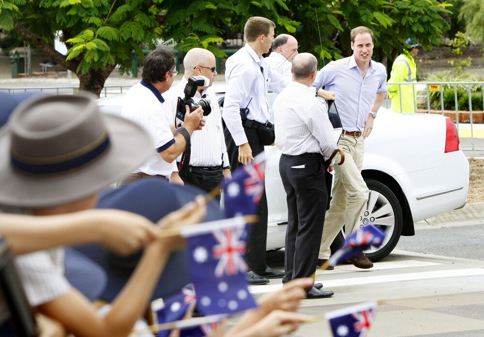 William, Prince of Wales, exiting car with dignitaries and security staff with students of West Moreton Anglican College waving flags, Karrabin, Ipswich, 2011