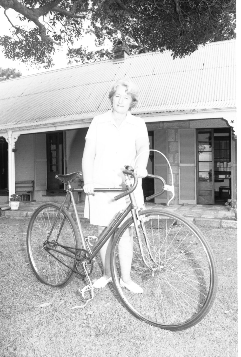Mrs Wass standing with an antique bicycle outside Wolston House, Wacol, Queensland, January 1978