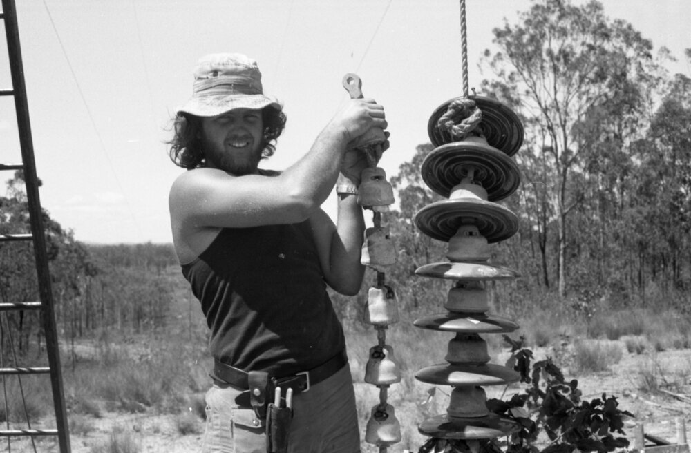 Man holding ceramic insulators from a power pole, Ipswich, December 1977