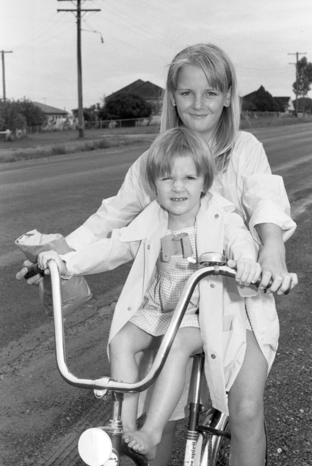 Unidentified children sitting on bicycle on the side of suburban road, Ipswich, February 1978