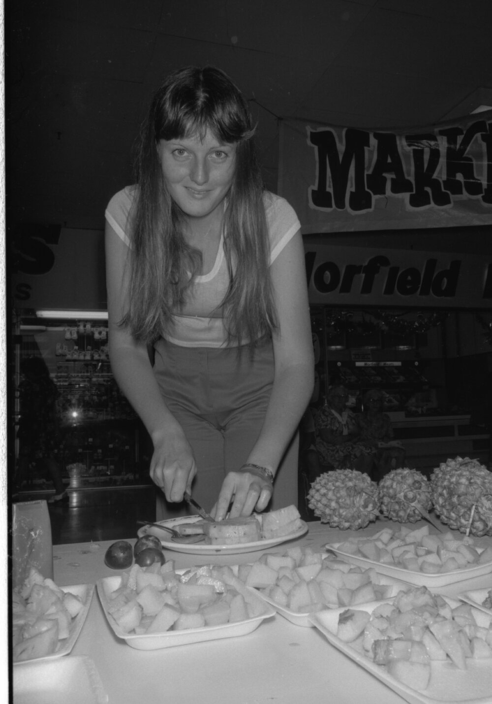 Unidentified woman preparing pineapple outside Morfield Meats in Booval Fair, Booval, Ipswich, February 1978