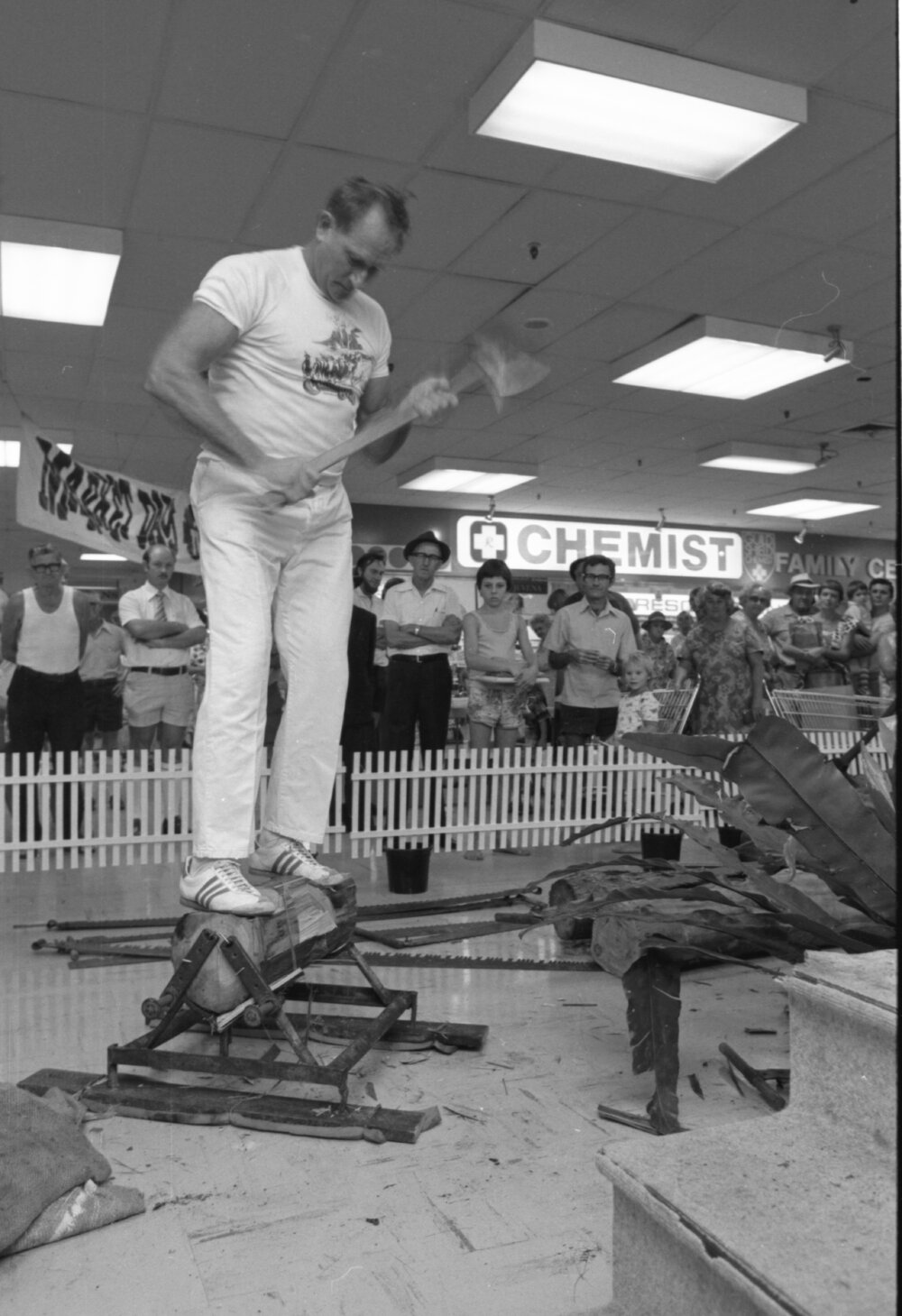 Unidentified man wearing Canungra shirt performing an underhand woodchopping demonstration with an axe in Booval Fair, Booval Ipswich, February 1978