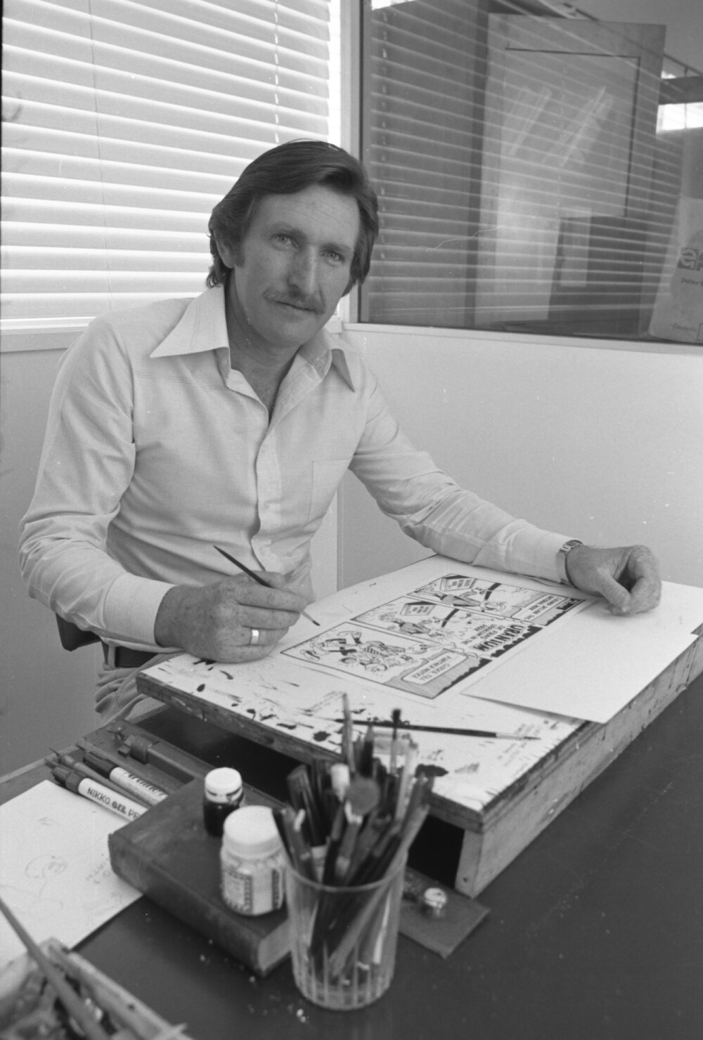 Queensland Times cartoonist Wil Mitchell working at his desk, Ipswich, Queensland, 1978