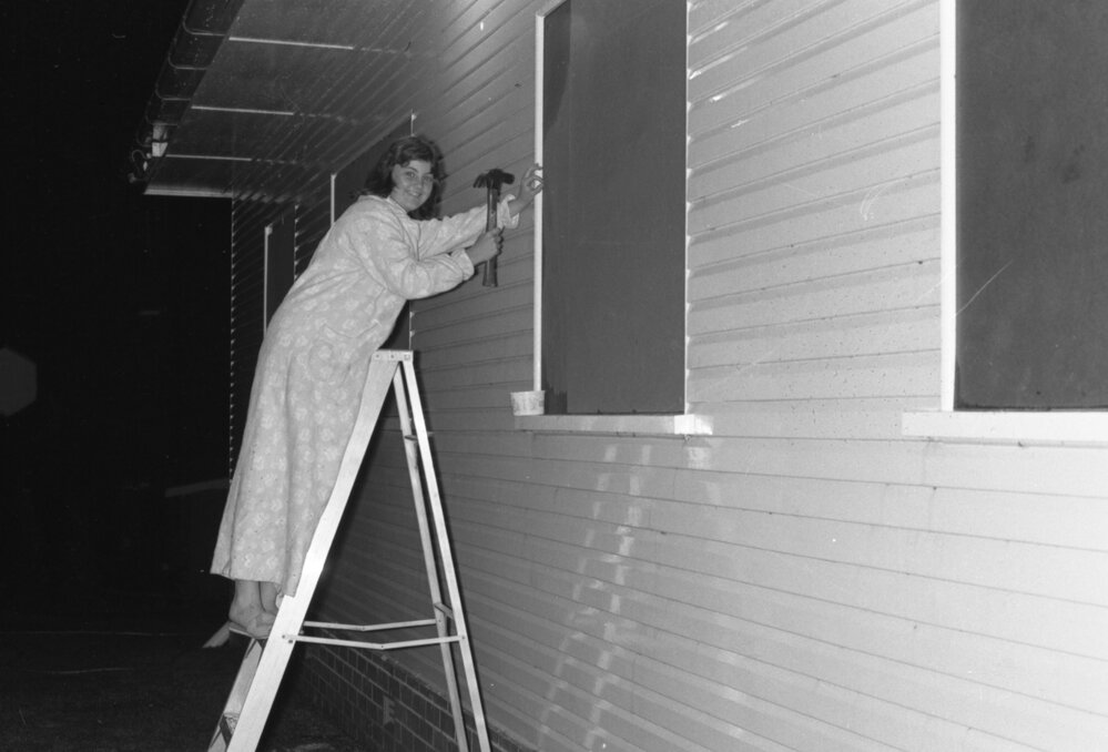 Woman boarding up windows after storm damage, Ipswich, November 1977