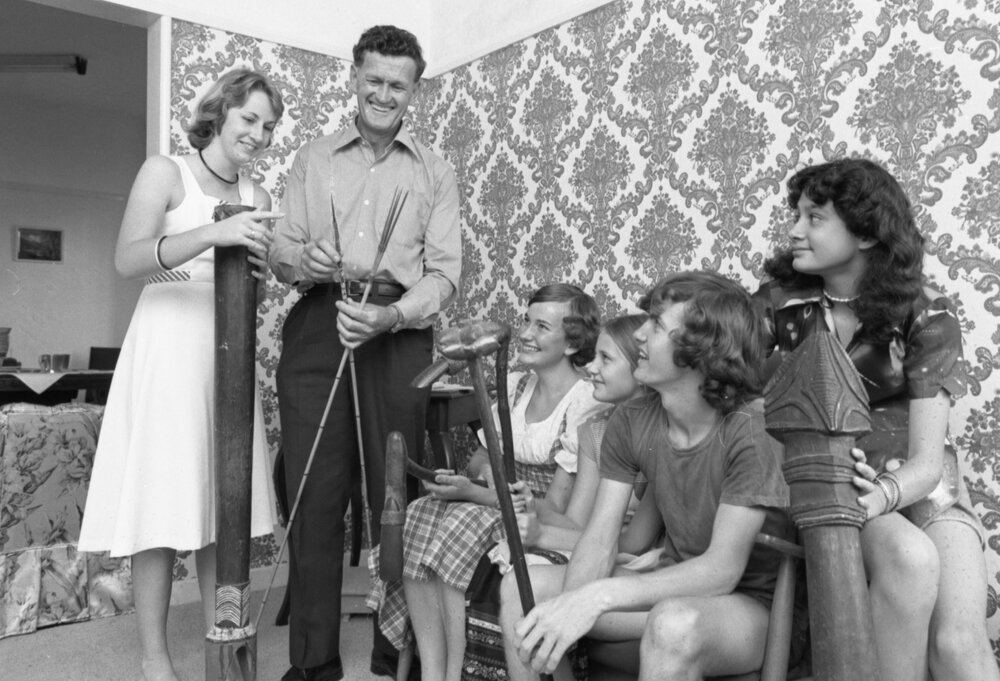 Unidentified family members examine indigenous implements or travel souvenirs in living room, Ipswich, November 1977