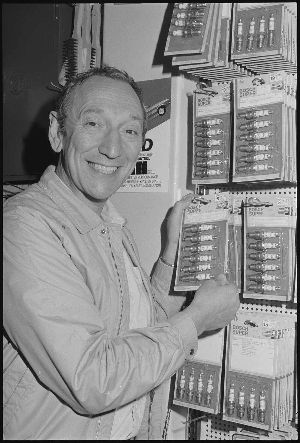 Man in shop with display of Bosch spark plugs and SAAS steering wheels, July  