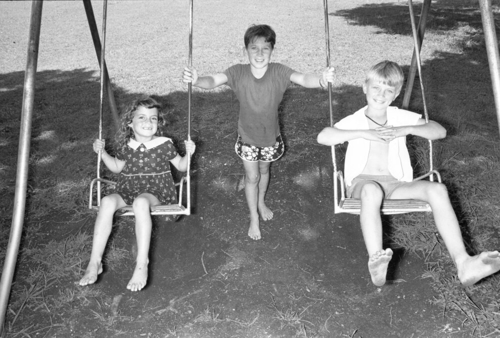 Three unidentified children playing on a swing set, Ipswich, Queensland, February 1978