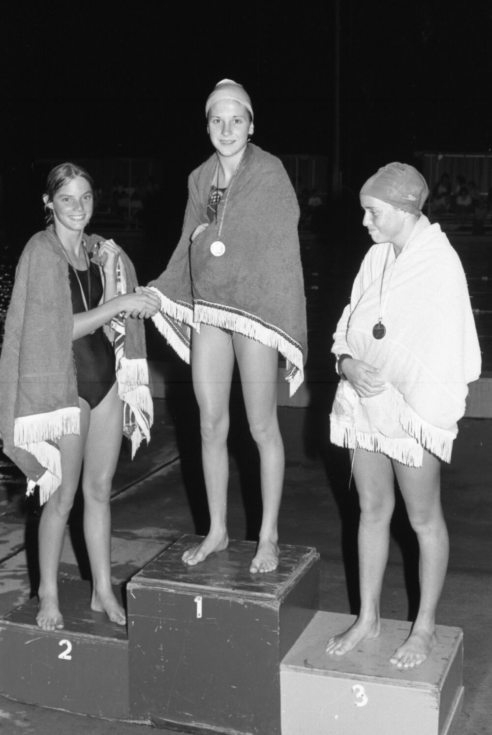 Three unidentified swimmers with medals on a podium, Ipswich, Queensland, February 1978