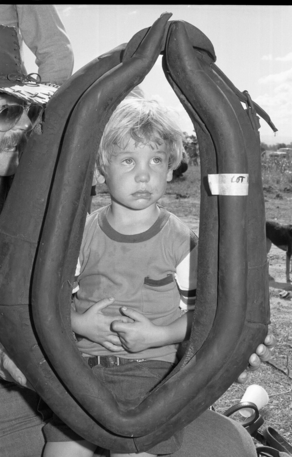 Unidentified little boy looking through a horse collar for sale at an unidentified horse event, Ipswich, February 1978