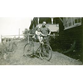 Young child on bicycle with her father at their home in Delacey Street, North Ipswich, 1949