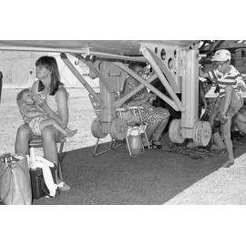 Women and children taking shelter under an aircraft at the RAAF Base, Amberley, December 1977
