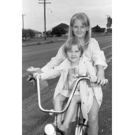 Unidentified children sitting on bicycle on the side of suburban road, Ipswich, February 1978