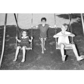 Three unidentified children playing on a swing set, Ipswich, Queensland, February 1978
