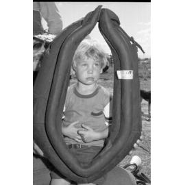Unidentified little boy looking through a horse collar for sale at an unidentified horse event, Ipswich, February 1978