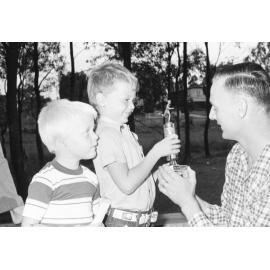 Daniel Hull receiving Little Athletics trophy from unidentified man with unidentified boy, Ipswich, Queensland