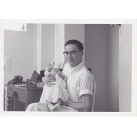 Doctor Chiu holding unidentified baby in office, Ipswich Hospital, Ipswich, 1950s