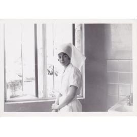 Sister Bernadette Smith (Tracey) at window by hand basin, 1950s