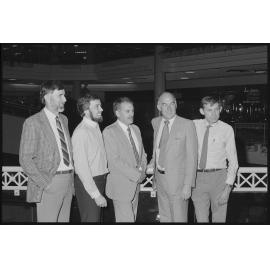 Unidentified group of men in business attire standing in front of the north escalator of Redbank Plaza Shopping Centre, Redbank, September 1985