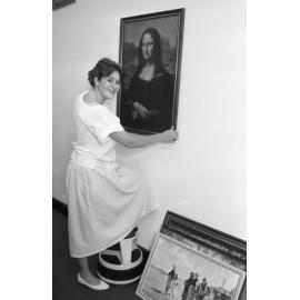 Unidentified library staff member hanging a poster of Leonardo da Vinci's 'Mona Lisa' in the Redbank Plaza Library, Redbank, September 1985