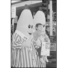 Bananas in Pyjamas are walking down Brisbane Street, Bananas in Pyjamas are carrying a small child, because in August 1994 the Variety Bash came to Ipswich